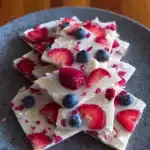 Healthy frozen yogurt bark topped with fruits and nuts on a white plate