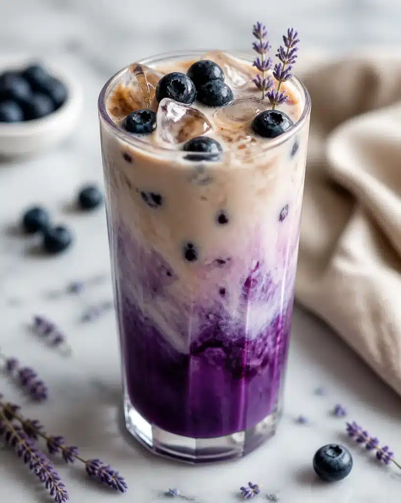 Blueberry and Lavender Oat Milk Latte topped with fresh blueberries and lavender flowers.