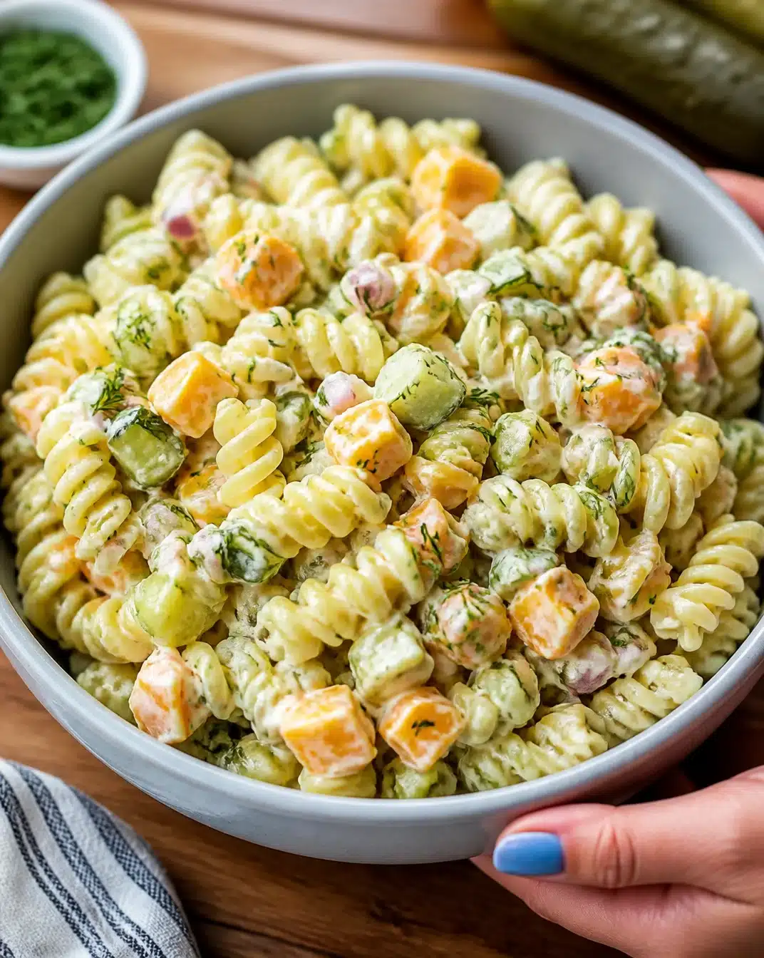 Bowl of dill pickle pasta salad garnished with fresh herbs and spices